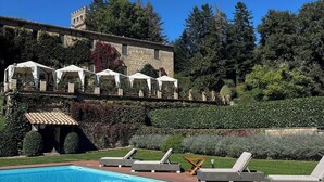 A swimming pool with lounge chairs, a stone building with a tiled roof, and a lush green garden. - Castello di Santa Cristina (Grotte di Castro)