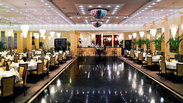 A spacious hotel lobby with a long reception desk, multiple dining tables, and chairs arranged on both sides of a central walkway. - Hotel Iskierka Business & Spa (Mielec)