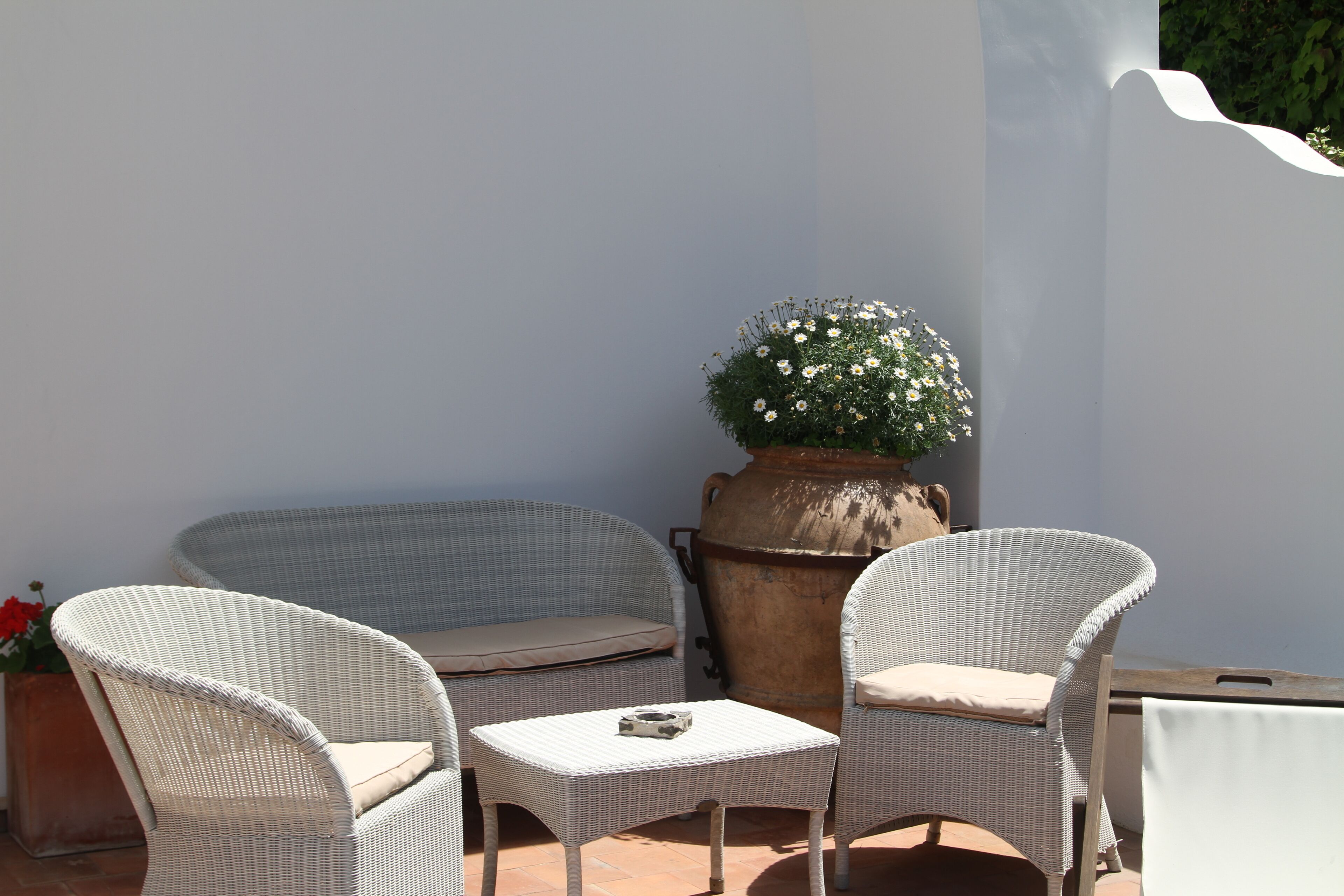 A patio area with wicker furniture, including a sofa and two chairs, a small table, and a large planter with flowers.