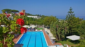 A swimming pool with lounge chairs and umbrellas, surrounded by greenery and buildings. - B&B Il Sogno (Anacapri)