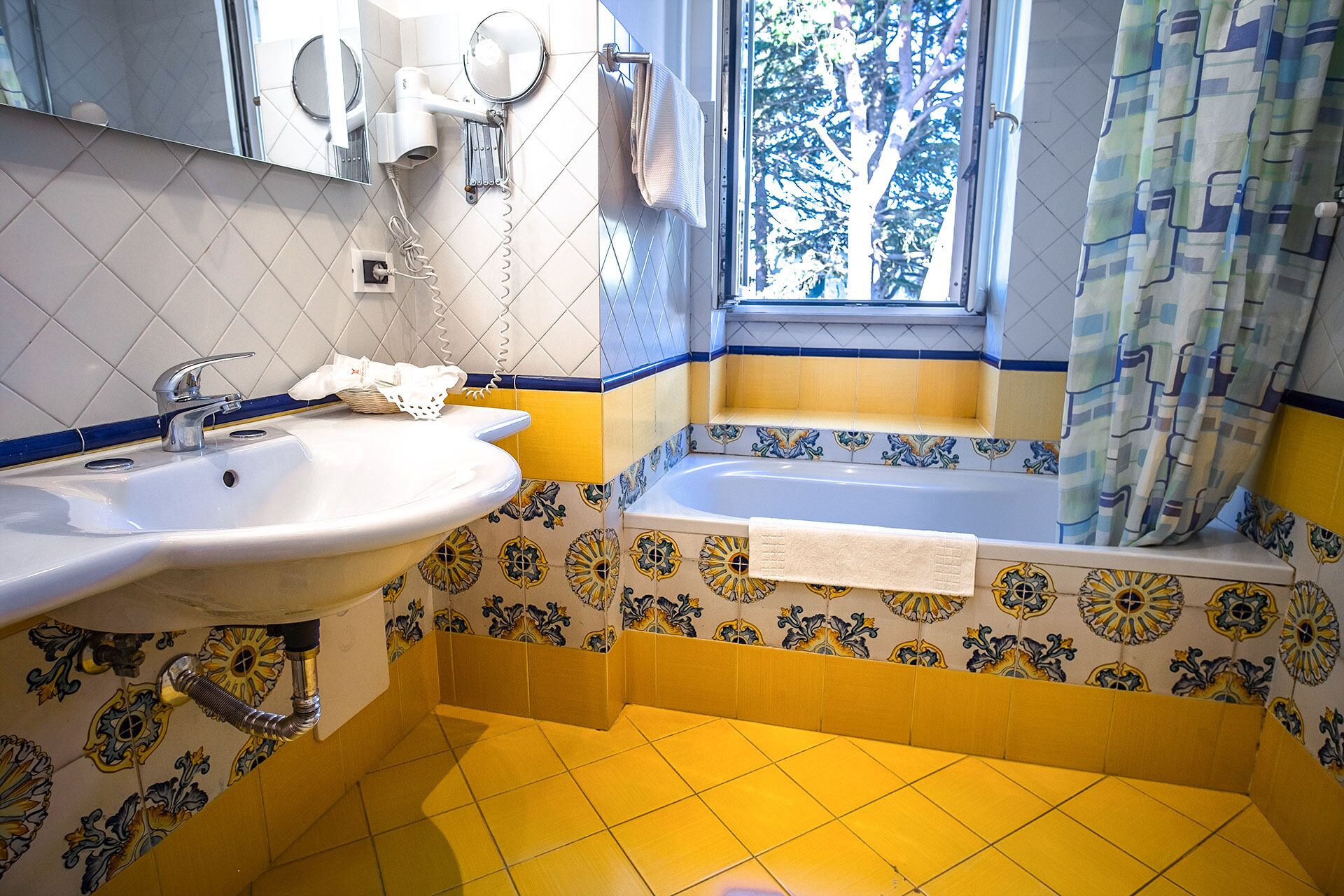 Un baño con lavamanos, espejo, secador de pelo y ventana con vistas a árboles.