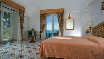 Une chambre d’hôtel avec un grand lit, une petite table sur laquelle est posé un vase, une chaise et une vue sur la mer, visible à travers une porte coulissante.