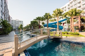 Una piscina con un puente, palmeras y un tobogán de agua.