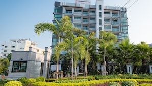 Un edificio moderno de varios pisos con fachada de vidrio, rodeado de vegetación cuidada y un cielo despejado.