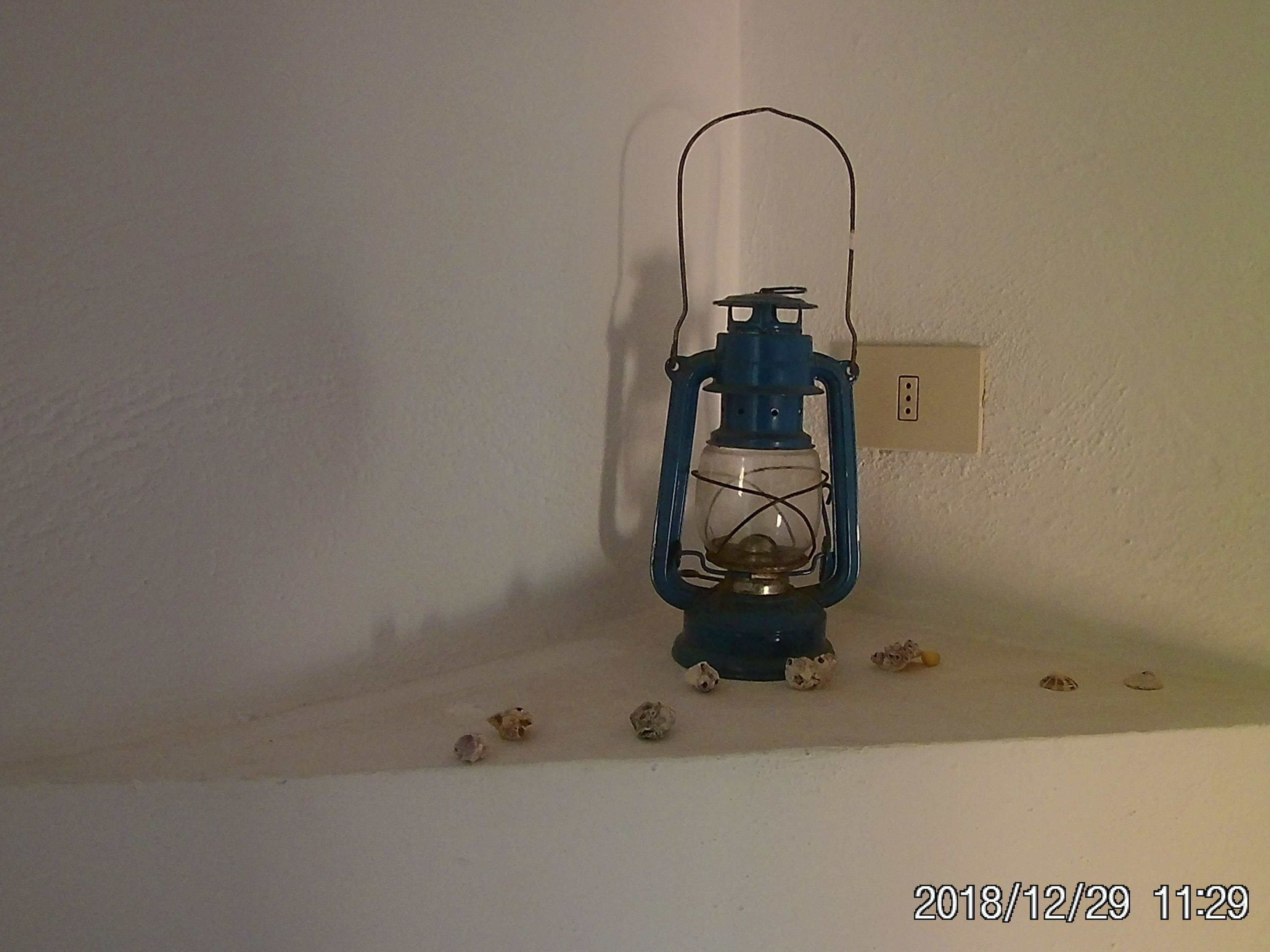 A blue lantern with a glass enclosure on a white wall, next to a power outlet.