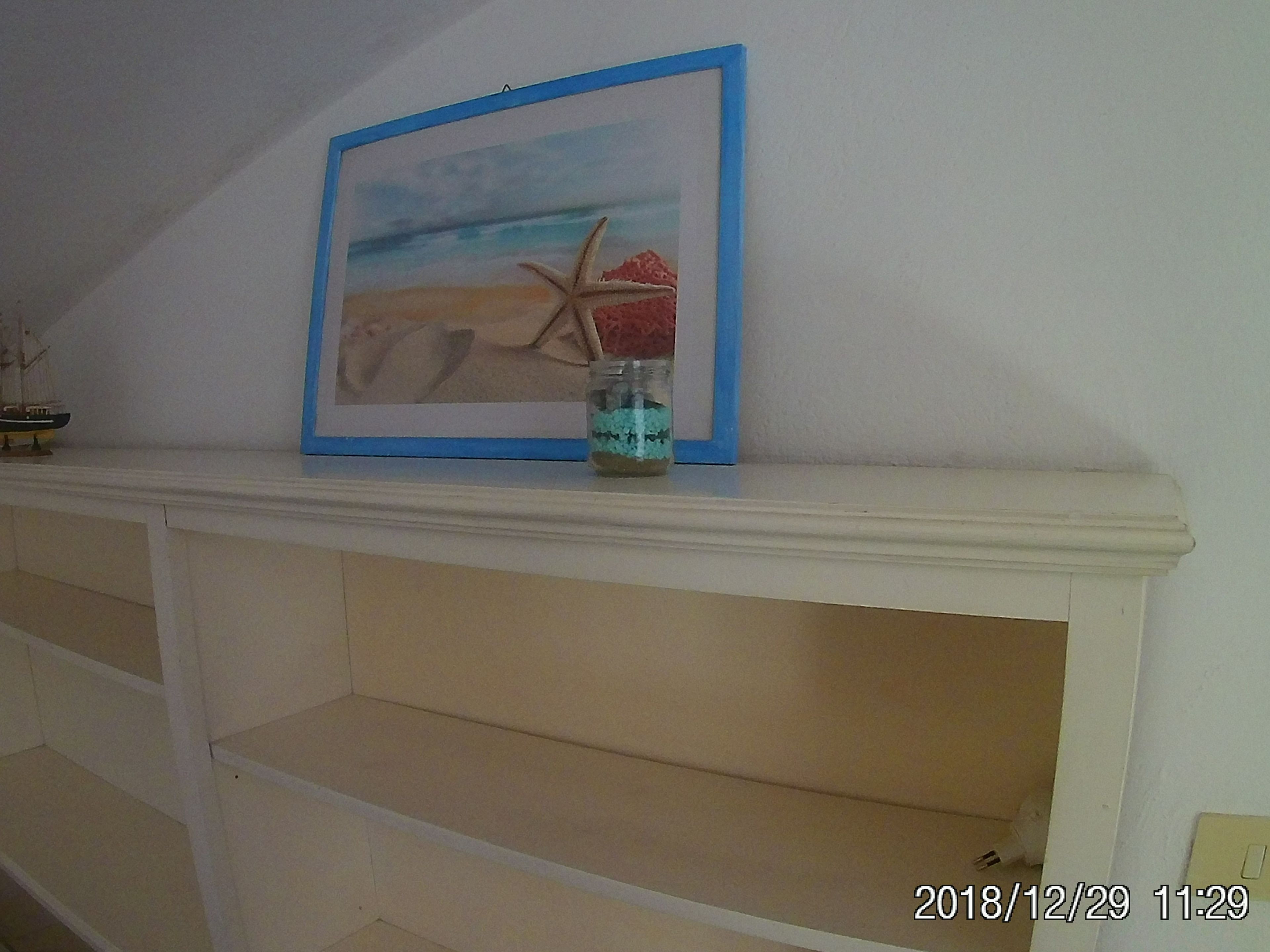 A framed painting of a beach scene with a starfish on a mantelpiece.