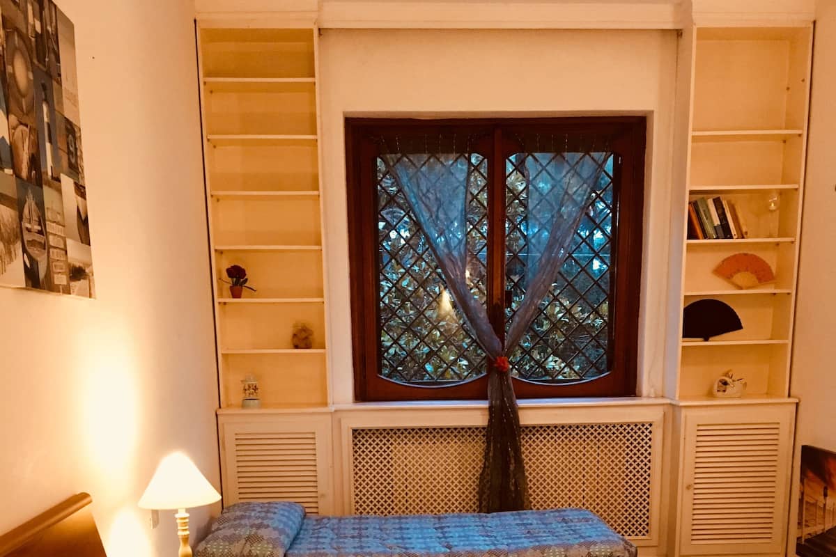 A bedroom with a bed, bedside tables, a window with a view, and built-in shelving.
