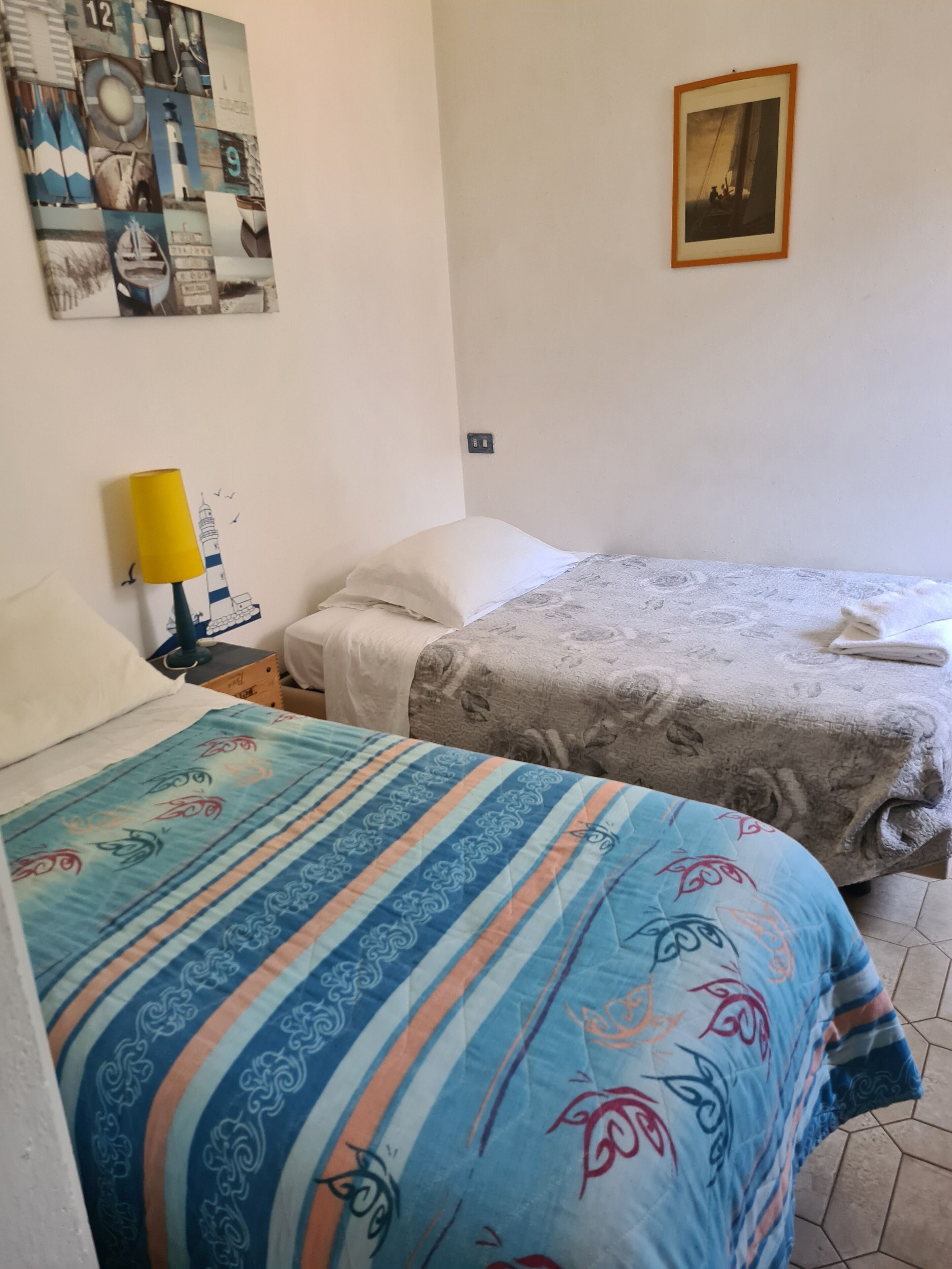 A hotel room with two beds, a painting on the wall, and a lamp.