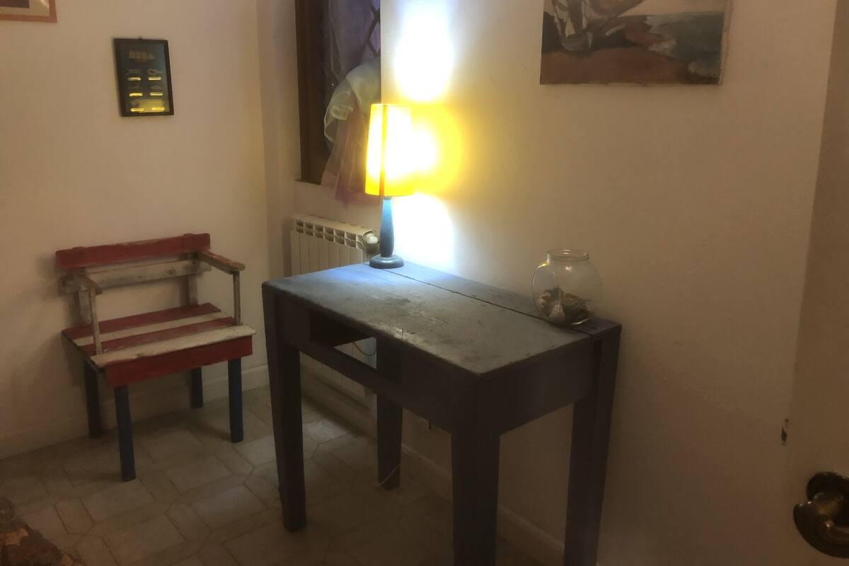 A small room with a wooden table, a bench, a lamp, and a painting on the wall.