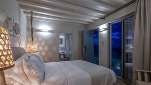 A bedroom with a bed, a hanging light fixture, and a view of the outside. - Oniro Suites (Mykonos)