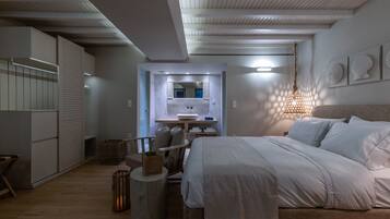 A modern bedroom with a bed, bedside table, and a mirror. There is a small seating area with a chair and a side table.