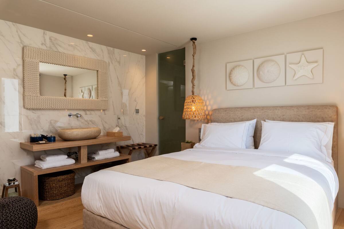 Quarto com cama grande, mesa de cabeceira de madeira, pia embutida e espelho.
