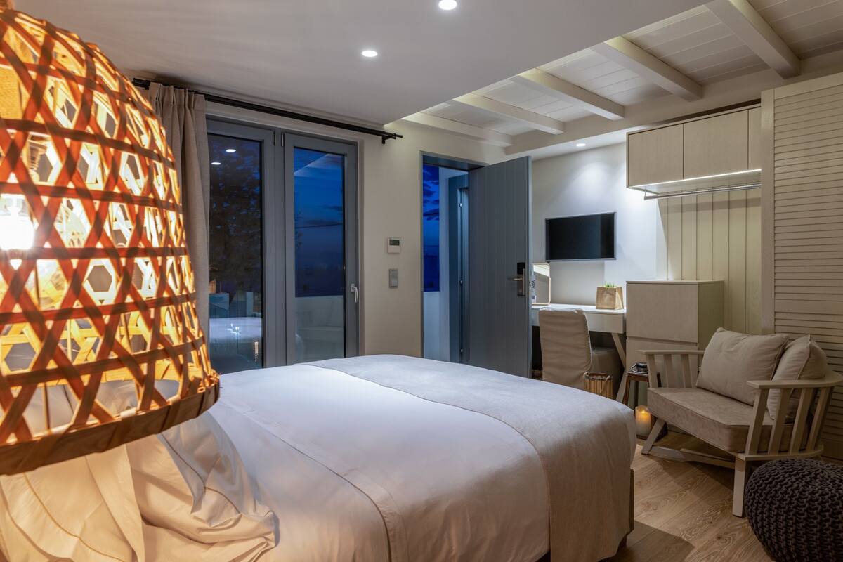 Quarto de hotel com cama, escrivaninha, cadeira, televisão e vista exterior.