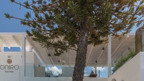 A modern hotel with a two-story structure, a glass staircase, and a tree in the courtyard. - Oniro Suites (Mykonos)
