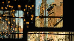 Una vista attraverso una finestra con luci sfocate, che mostra un edificio in mattoni e una scena di strada.