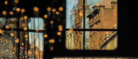 Vista a través de una ventana con luces desenfocadas, que muestra un edificio de ladrillo y una escena callejera.