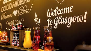 En væg med skilte, der siger "Welcome to Glasgow!" og "Good Morning", samt et udvalg af farverige drikkevarer og syltetøjsglas.