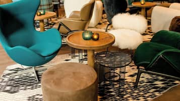A modern lounge area with various seating options including a teal armchair, a round wooden table, and a small black metal table.