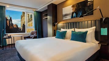 Ein Hotelzimmer mit einem großen Bett, Blick auf eine Stadtkulisse durch ein Fenster, einem kleinen Tisch mit einem Stuhl und einer Wandlampe.