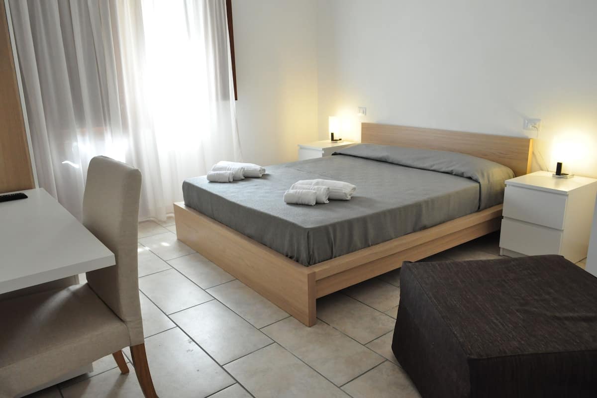Una habitación de hotel moderna con una cama de madera, un escritorio y una silla. Hay dos mesitas de noche con lámparas.