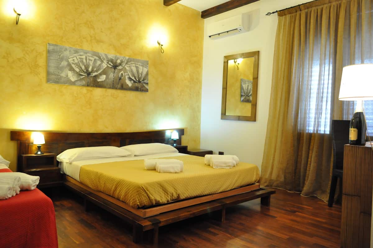 Una habitación de hotel con una cama grande, dos mesitas de noche con lámparas, un espejo y un banco de madera.