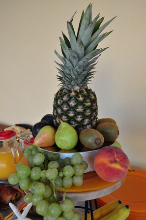 A fruit bowl with a pineapple, grapes, peaches, and other fruits. - Zefiro Rooms & Breakfast (San Vito Lo Capo)