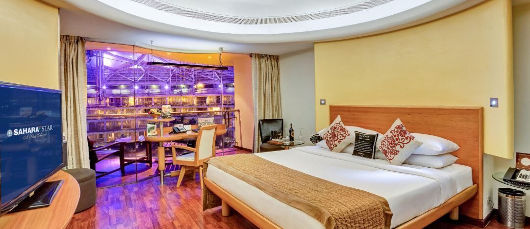A hotel room with a large bed, a desk with a chair, a TV, and a minibar.