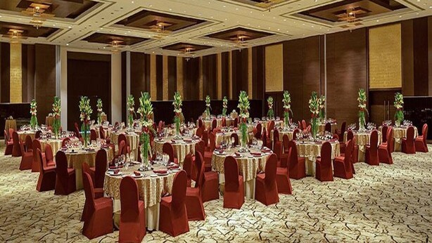 A banquet hall with round tables, red chairs, and floral centerpieces. - Sahara Star (Mumbai)
