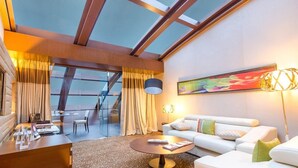 A modern hotel room with a glass ceiling, a sofa, a coffee table, a desk with a laptop, and a dining area with a table and chairs. - Sahara Star (Mumbai)