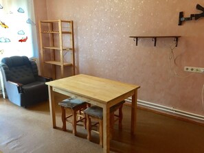 Une pièce comprenant une table en bois, deux chaises assorties, un fauteuil noir, une échelle en bois et une étagère fixée au mur.