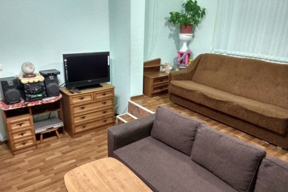 Un salon avec un canapé marron, une table basse en bois, un téléviseur posé sur un meuble et un système de haut-parleurs.