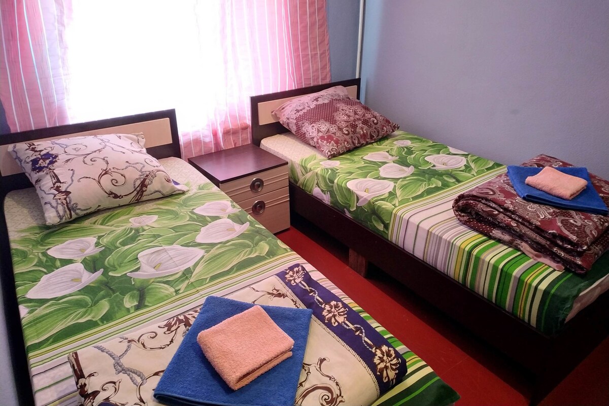 Une chambre avec deux lits simples, chacun agrémenté de draps à motifs floraux, d’une table de chevet et d’un tiroir.