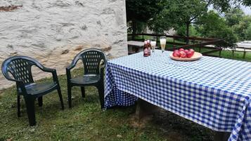 Ein Tisch im Freien mit karierter Tischdecke, zwei Plastikstühlen, einer Flasche, einem Glas und einer Obstplatte.