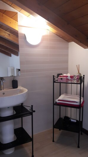 A bathroom with a white sink, a mirror, and a towel rack with folded towels. - B&B Lake Como Cottage (Lecco)