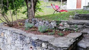 A stone wall with a garden bed, a tree, and a red chair in the background. - B&B Lake Como Cottage (Lecco)