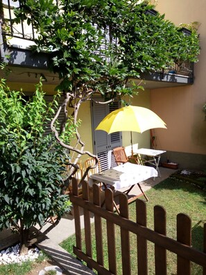 A patio with a table and chairs, a yellow umbrella, and a wooden fence. - B&B Lake Como Cottage (Lecco)