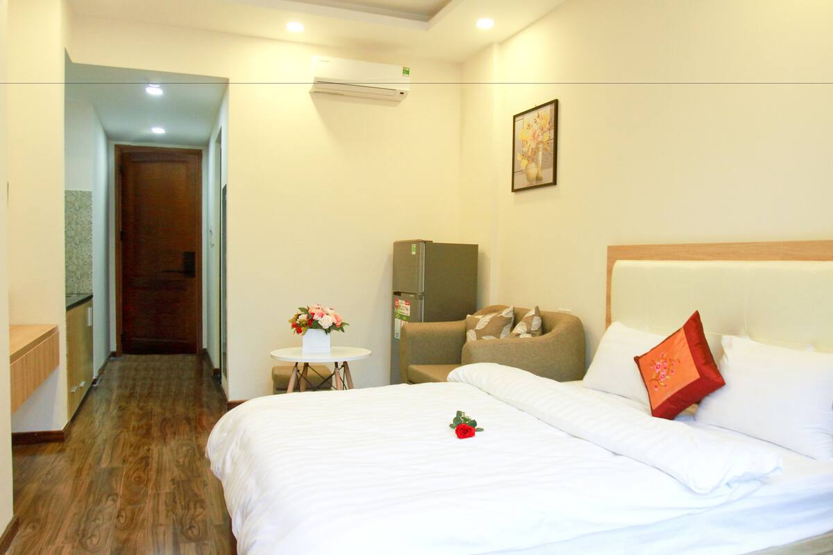 A hotel room with a bed, a small table with a vase of flowers, a refrigerator, and a sofa.