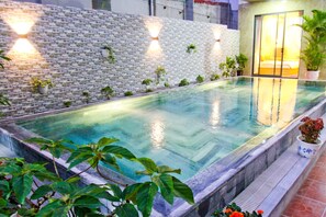 A rectangular swimming pool with a stone wall and potted plants on one side.