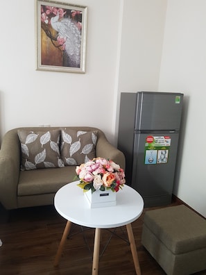 A living room with a sofa, a small round table with a floral arrangement, and a refrigerator.