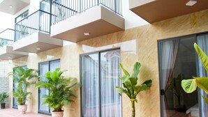 Exterior de un hotel con un patio de baldosas, plantas en macetas y un balcón.