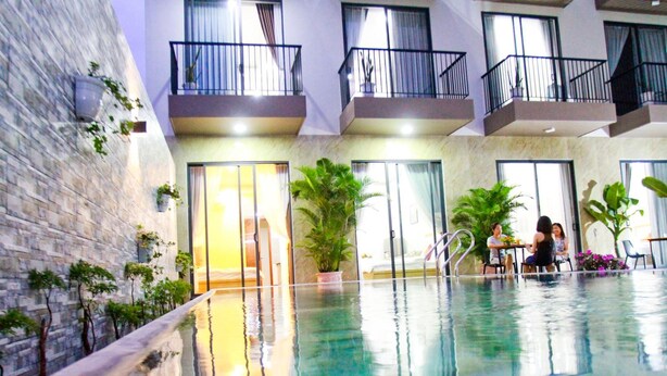Una piscina interior con agua cristalina, rodeada de plantas en macetas y una pared de piedra.