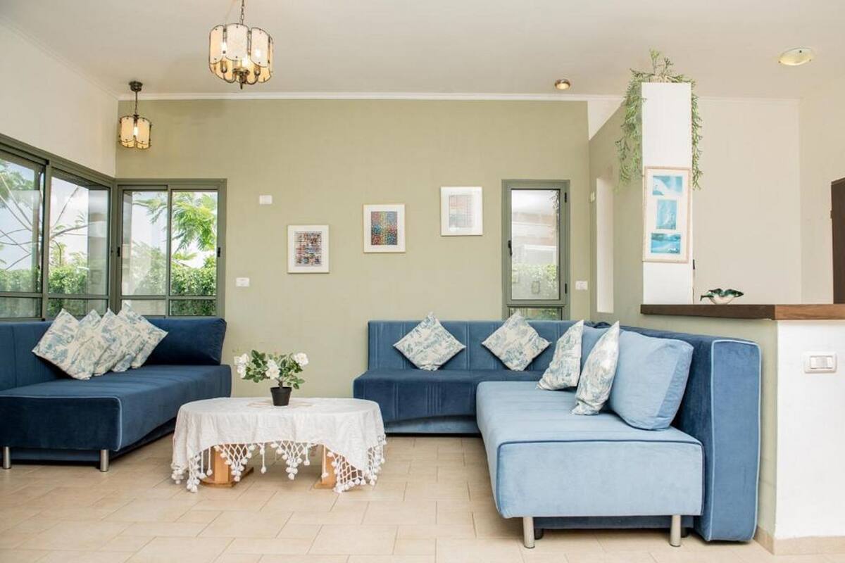 Un salon avec deux canapés bleus, une table blanche recouverte d’une nappe en dentelle et une plante posée sur un meuble.