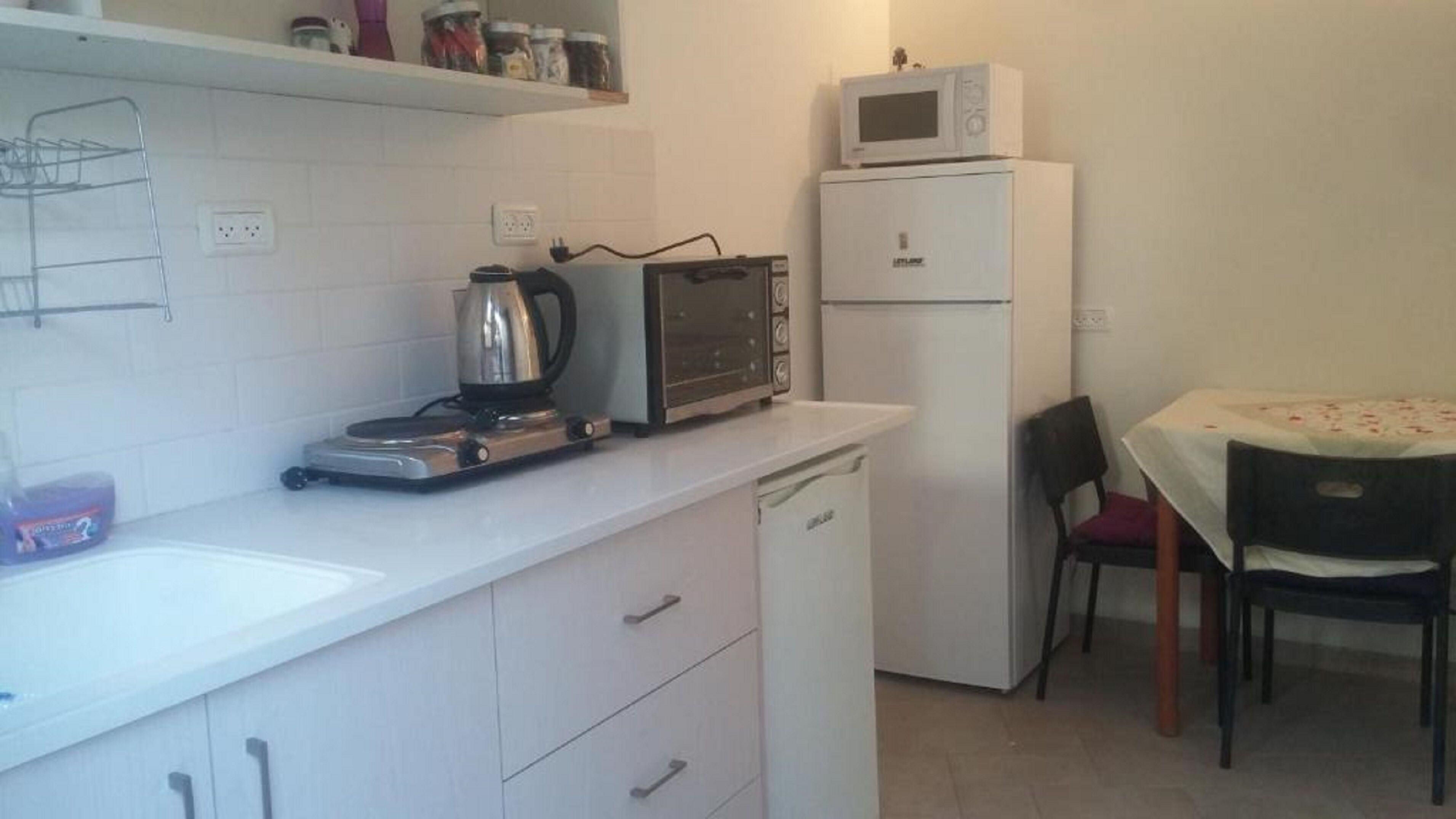A compact kitchen with a microwave, toaster, kettle, and a small refrigerator.