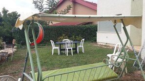 Un patio con un columpio, una mesa con sillas y una parrilla.