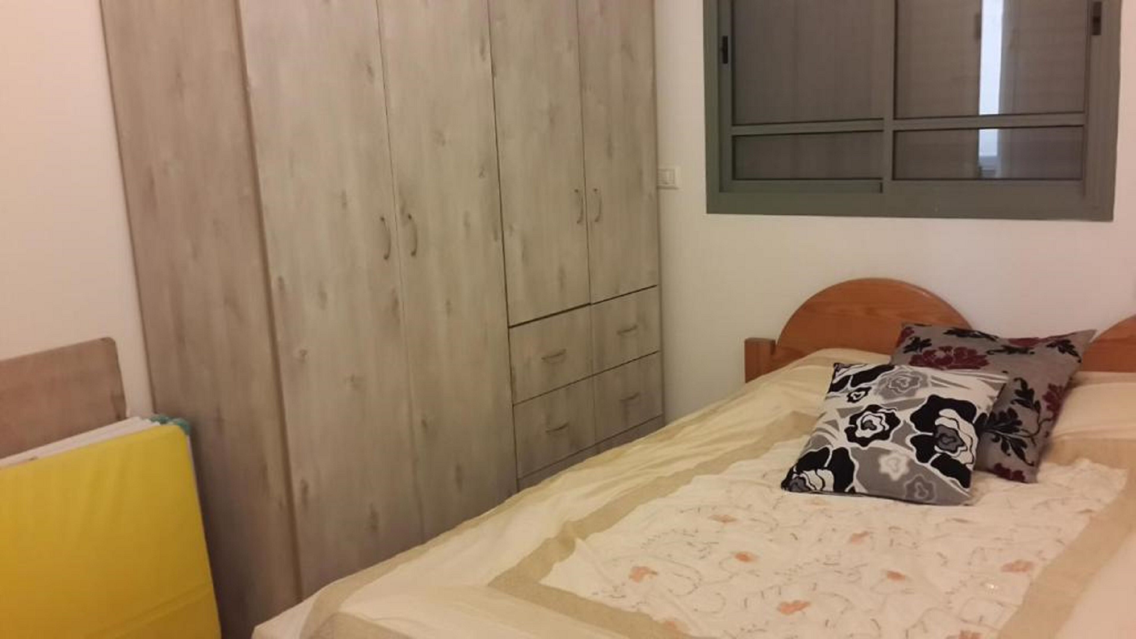 A bedroom with a bed, a wooden wardrobe, and a window.