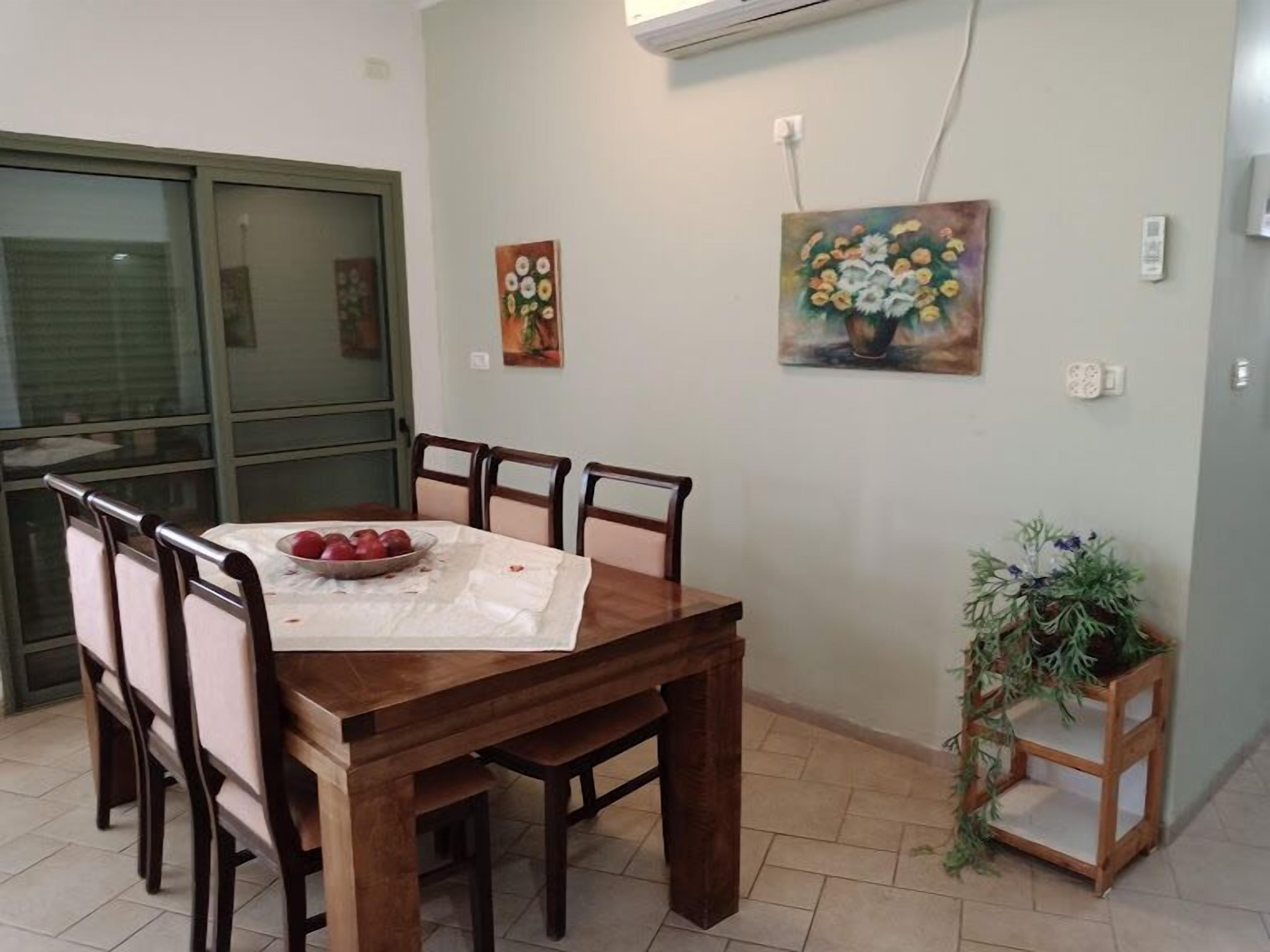A dining area with a wooden table and chairs, a bowl of fruit, and a potted plant.