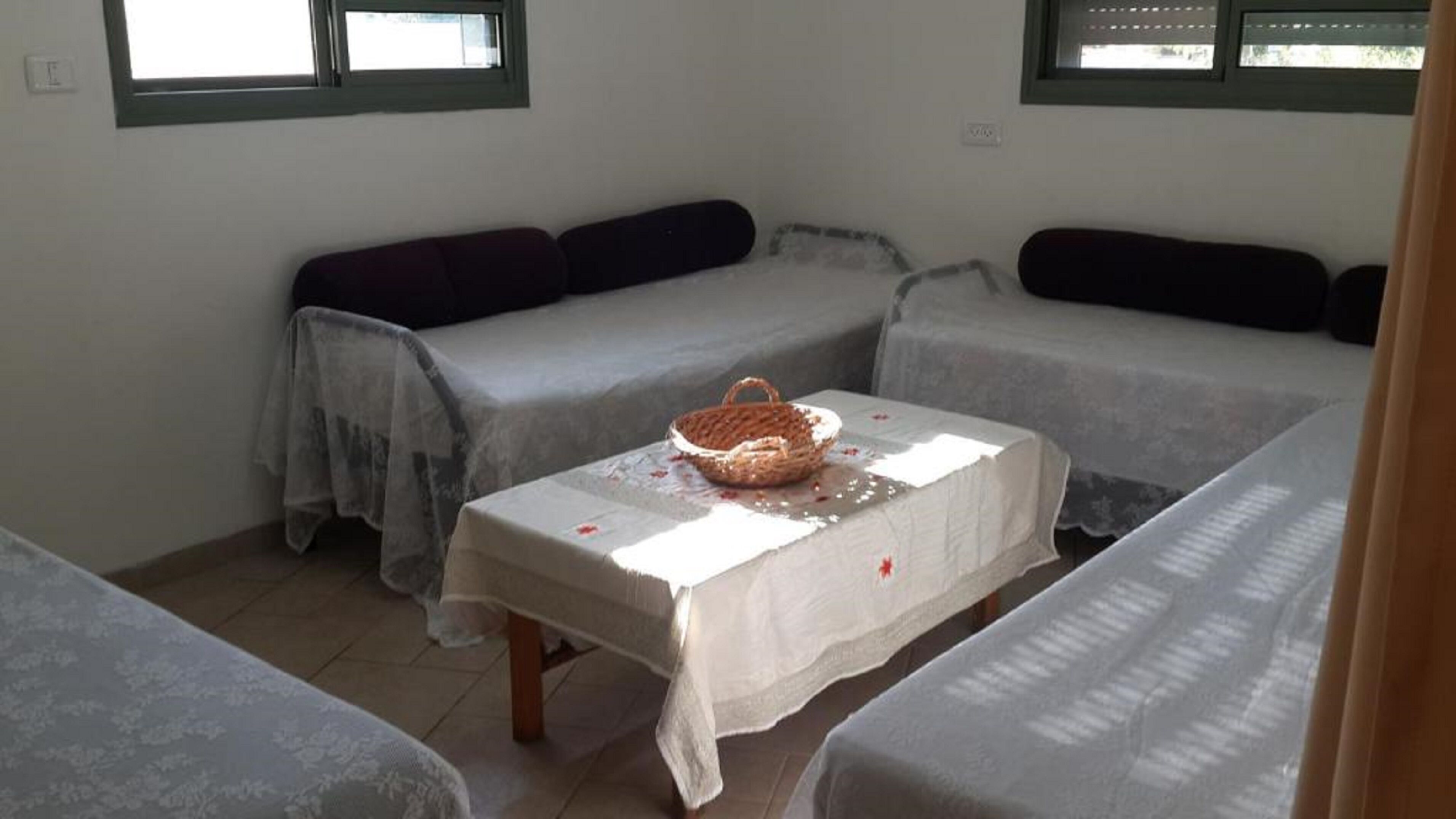 A room with two beds, a table with a basket, and a window.