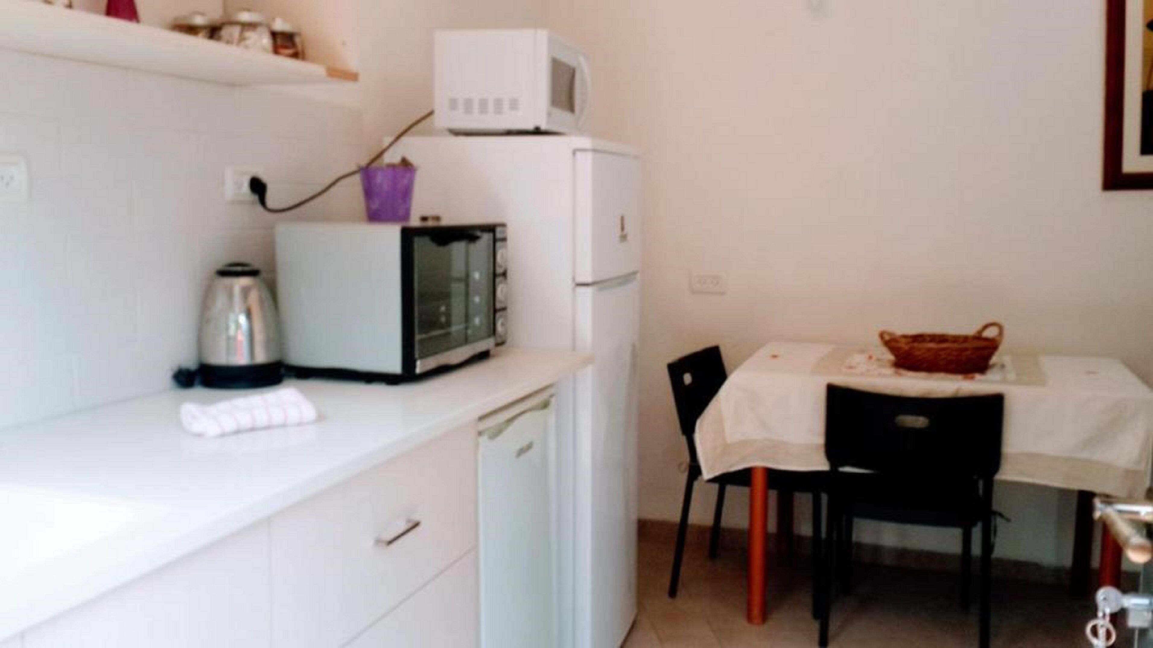 Eine kompakte Küche mit Mikrowelle, Toaster und Wasserkocher auf der Arbeitsfläche, einem kleinen Kühlschrank und einem Esstisch mit Stühlen.