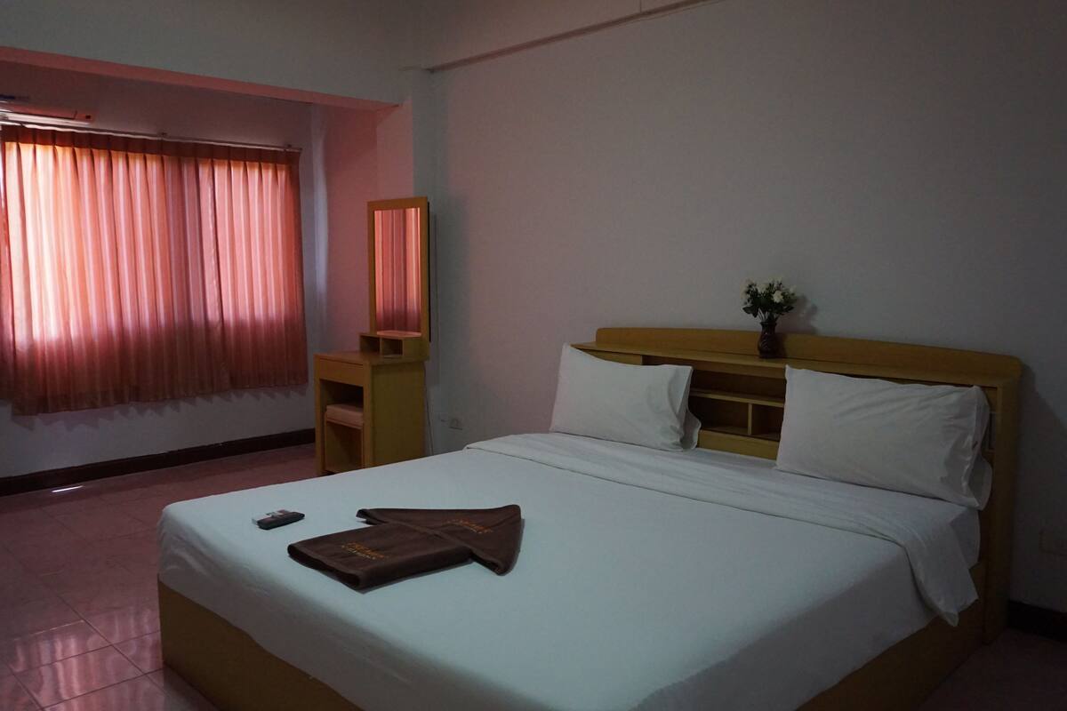 A hotel room with a bed, a bedside table, a mirror, and a window with curtains.