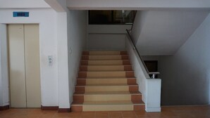 A staircase with a handrail, a closed elevator door, and a digital display above the elevator. - Premier Hotel Nakhonsithammarat (Nakhon Si Thammarat)